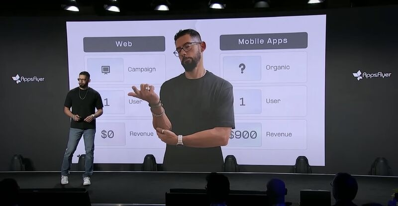 Gil Bouhnick on stage beside a presentation contrasting web and mobile measurement