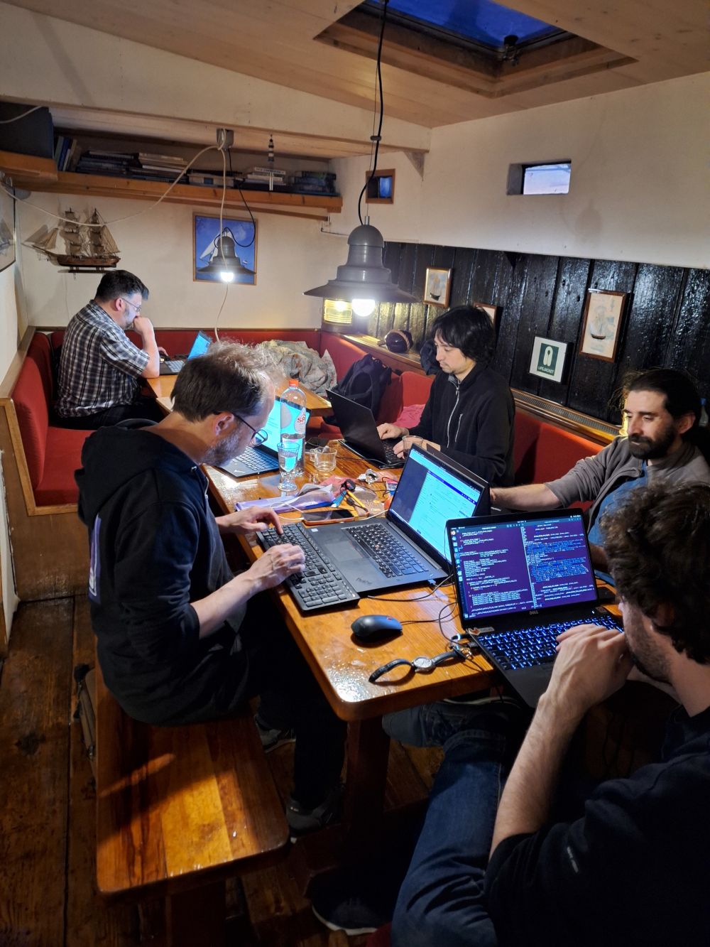 GIMP and Inkscape contributors working on laptops around a wooden table inside a sailing boat