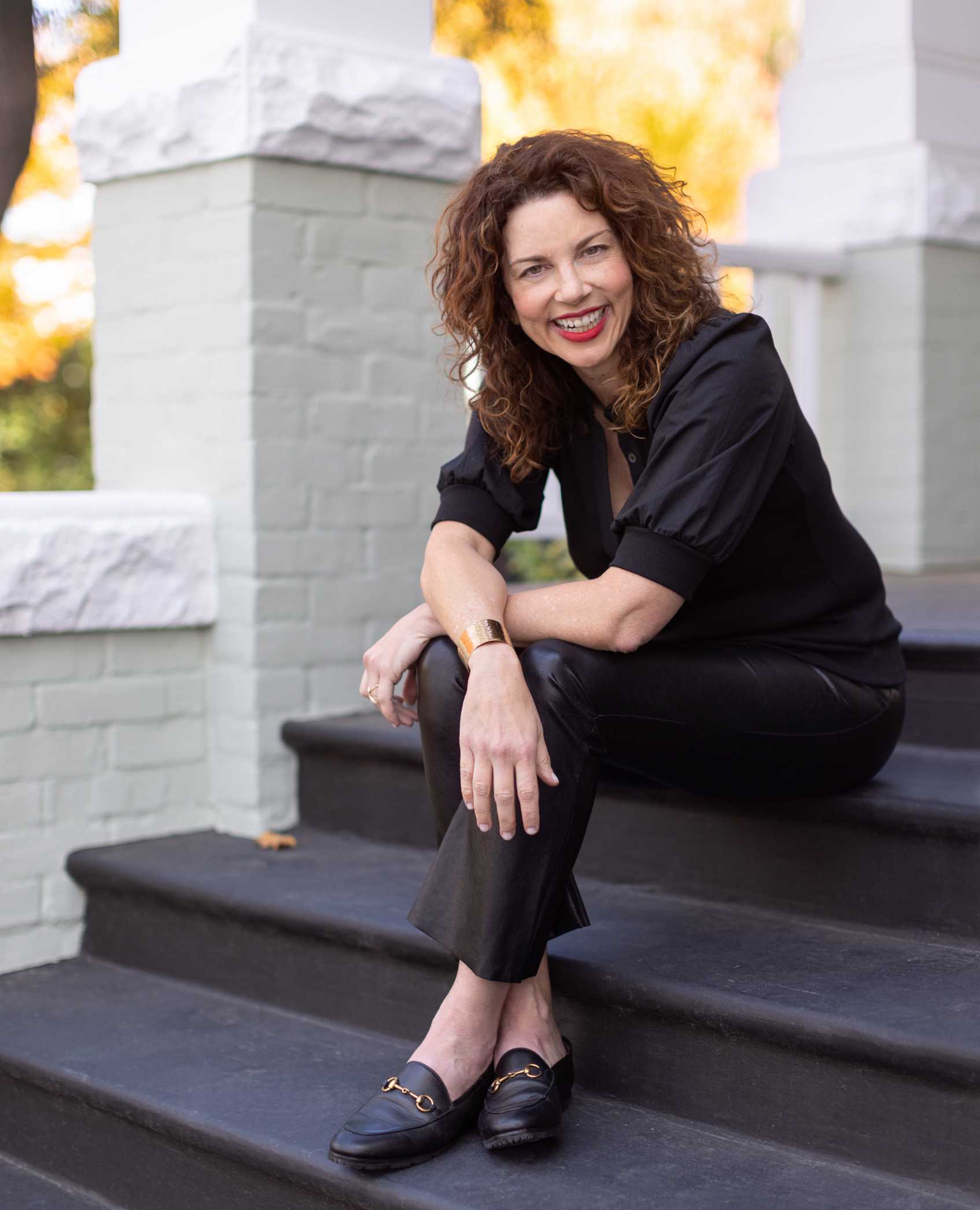 Gina Bianchini seated on outdoor steps, smiling, in an author publicity photograph