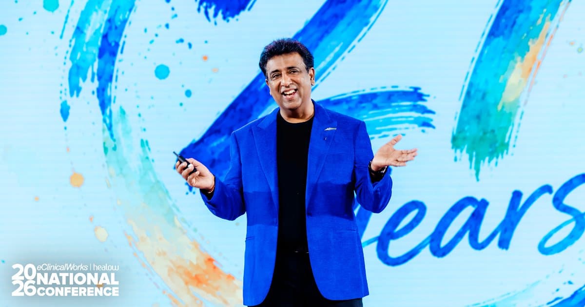 Girish Navani speaking onstage in a blue jacket at the 2026 eClinicalWorks and healow National Conference
