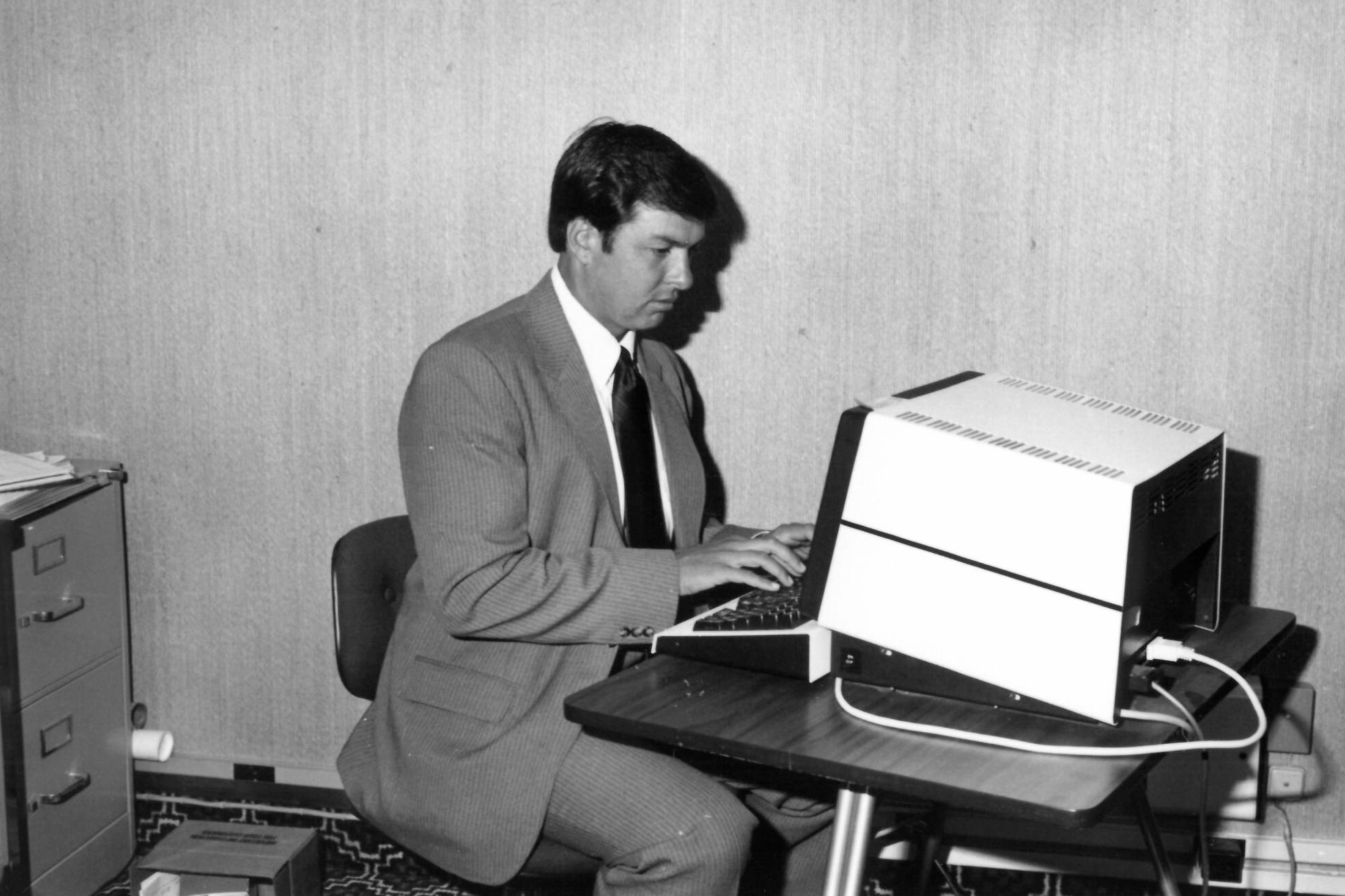 An archival office photograph showing a worker at a large desktop computer