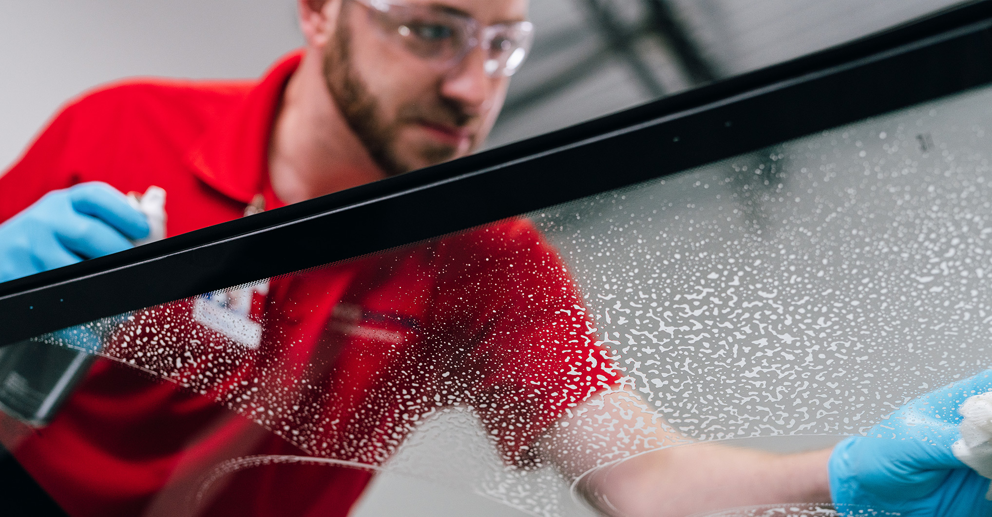 A glass service professional in safety glasses and blue gloves works on a large glass panel