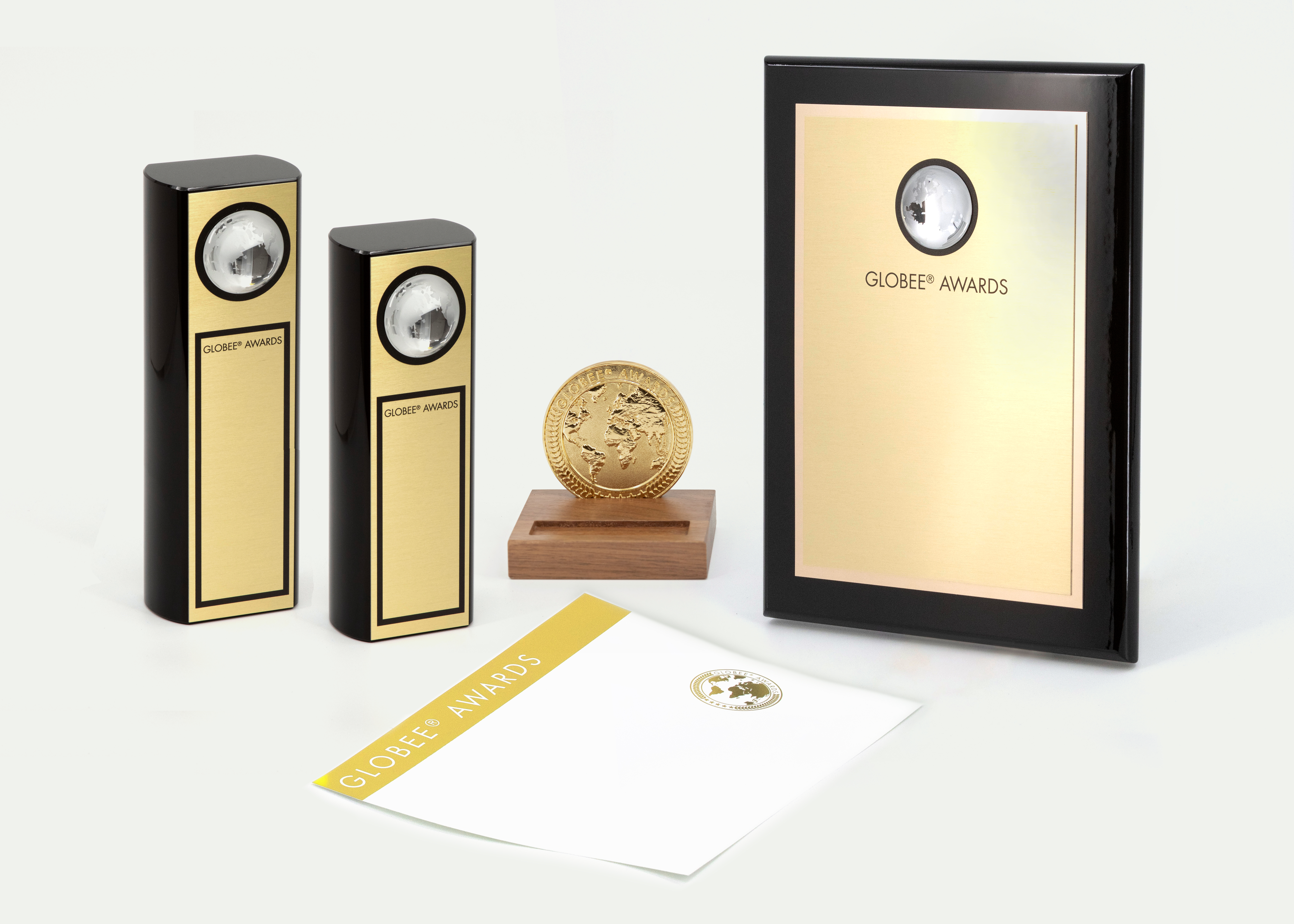 Official Globee product photograph with two gold-faced trophies, a medallion, plaque, and certificate