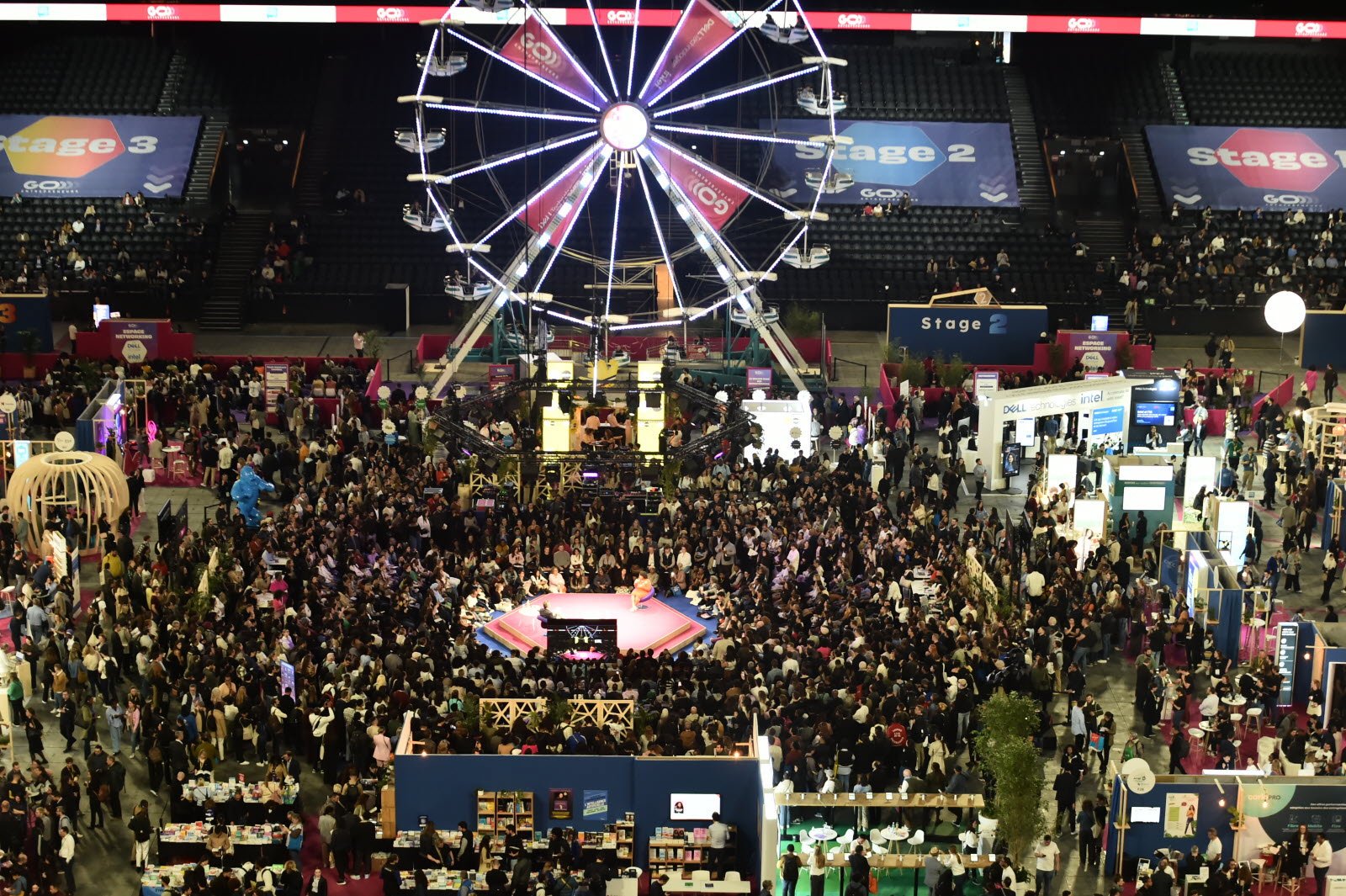 A Ferris wheel above a crowded exhibition floor and central pink stage at GO Entrepreneurs Paris 2025