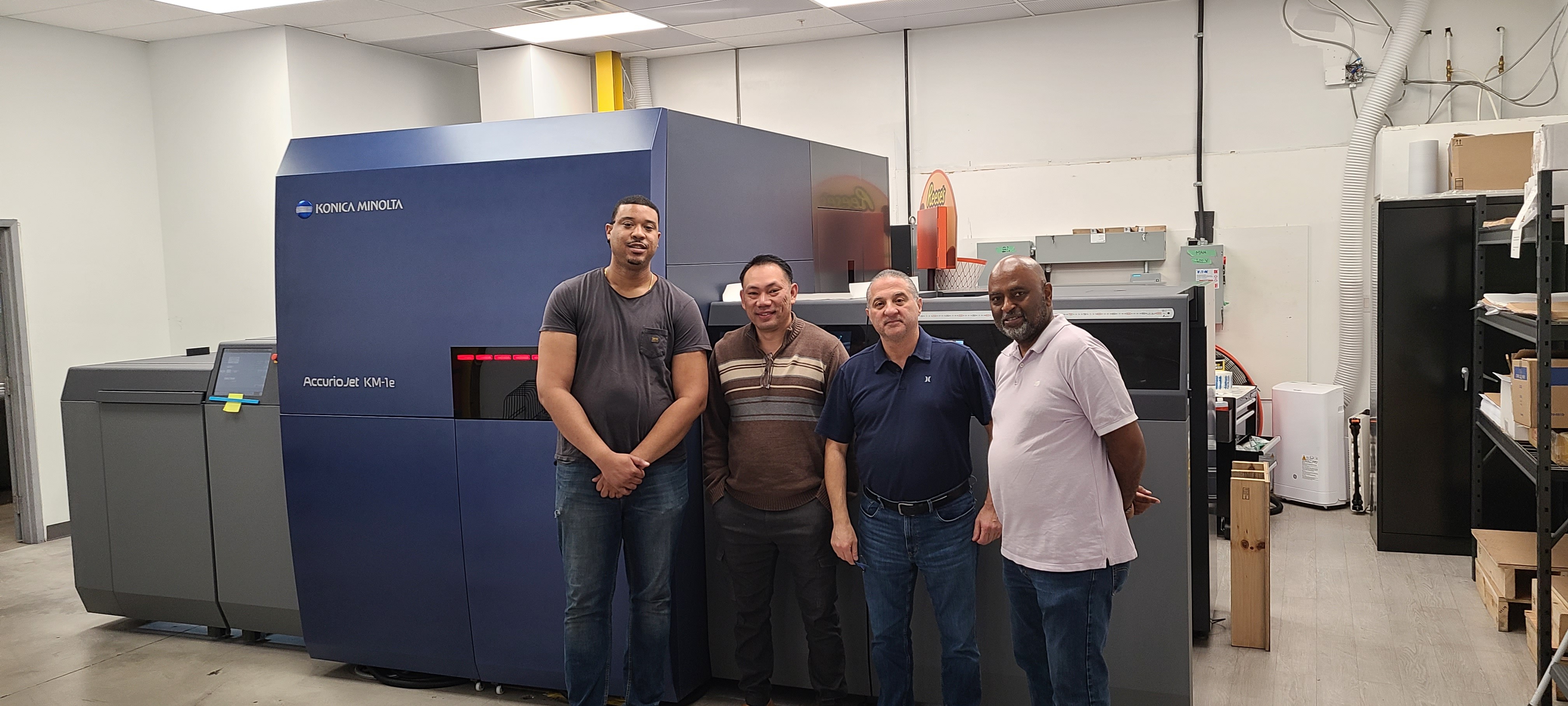 Four production staff standing in front of Godin's Konica Minolta AccurioJet KM-1e HD press