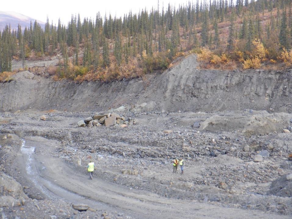 Three field visitors inspect an exposed gravel bank at the Chandalar placer mine