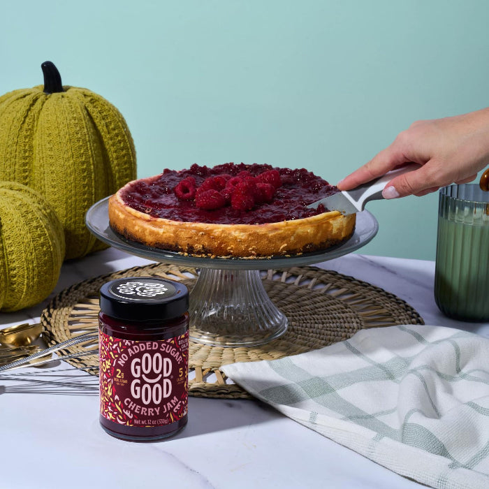 A jar of GOOD GOOD cherry jam beside a raspberry-topped cake