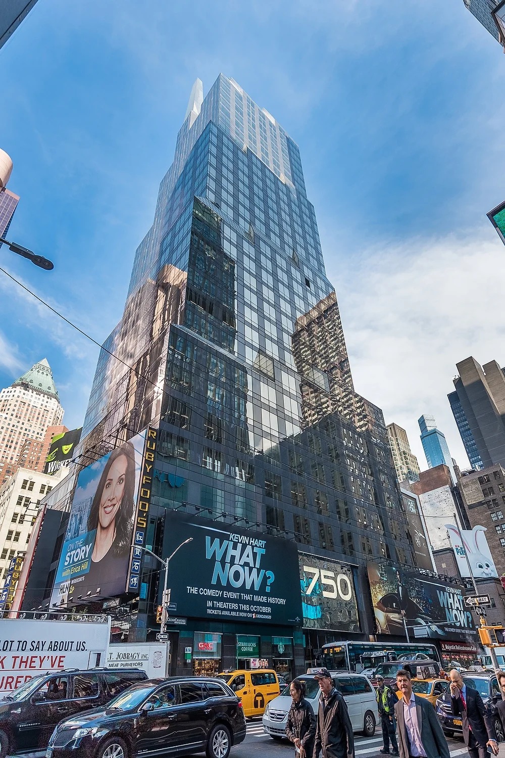 A street-level view looking up at a glass tower and billboards in Times Square, New York