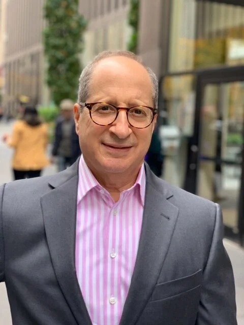 Tom Goodman in a gray jacket and pink striped shirt on a New York sidewalk
