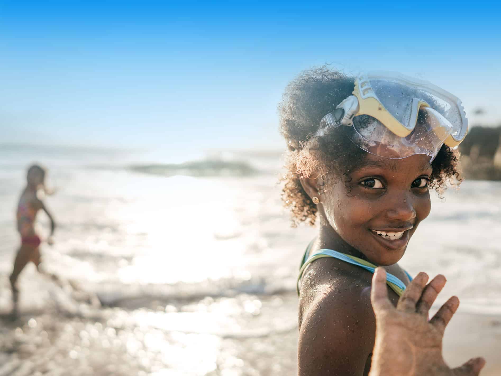 A smiling child with swimming goggles at the beach, in imagery from the Heartwired ocean project