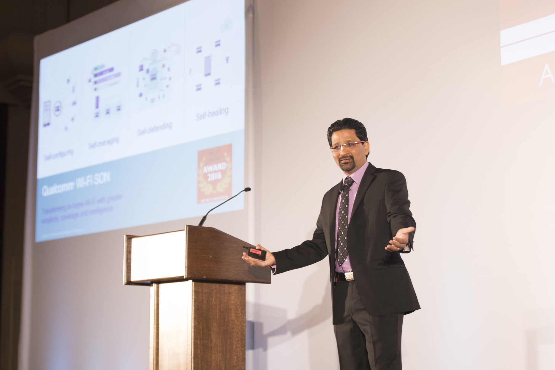 Gopi Sirineni presenting Wi-Fi SON beside a lectern and a projected network diagram