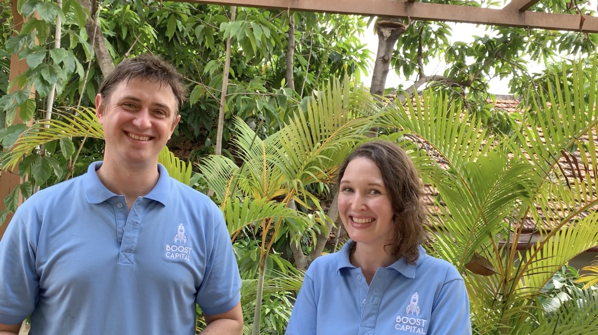 Gordon Peters and Lucinda Revell in blue Boost Capital polo shirts, standing outdoors among palms