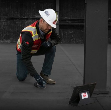 A GPRS technician kneels on a concrete floor, moving a scanner beside a laptop