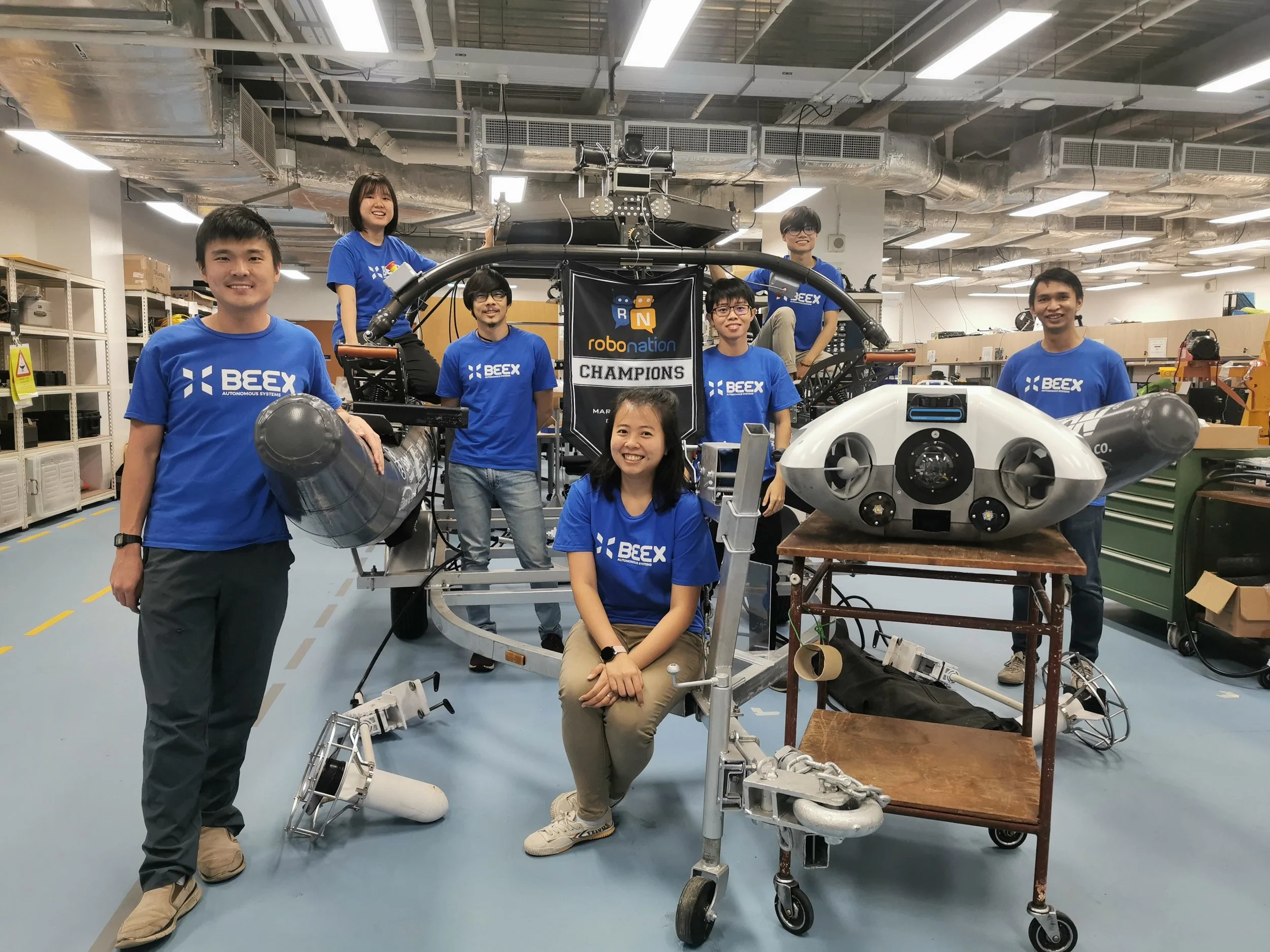 Grace Chia seated with BeeX colleagues and marine robotics equipment in a workshop