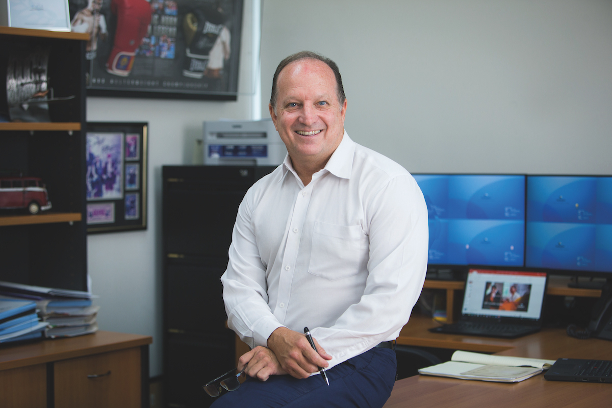 Graham Campbell seated beside a desk in an office, holding glasses and a pen
