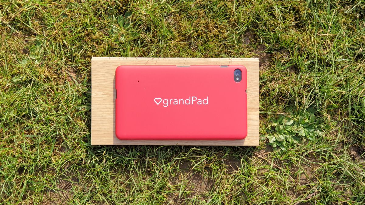 A red GrandPad tablet standing outdoors with the company logo visible on its back