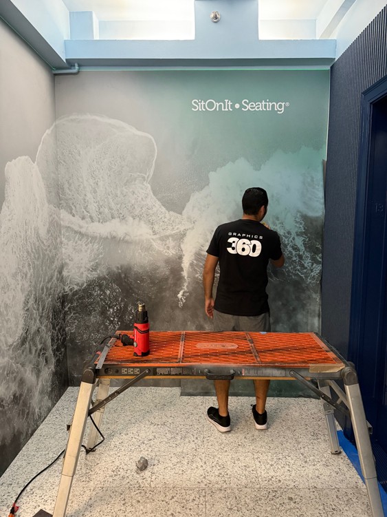 Graphics360 worker installing ocean-wave wall graphics in a SitOnIt Seating elevator lobby