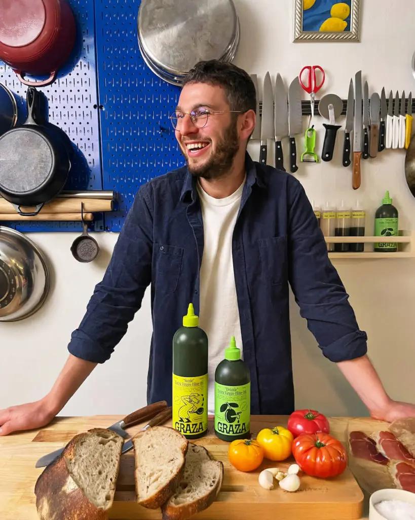 Graza co-founder Andrew Benin smiling beside bottles of olive oil