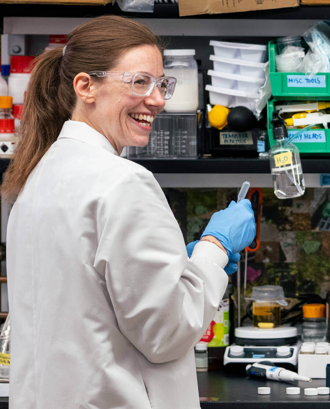 A Greentown wet-lab member wearing a lab coat, protective glasses, and blue gloves
