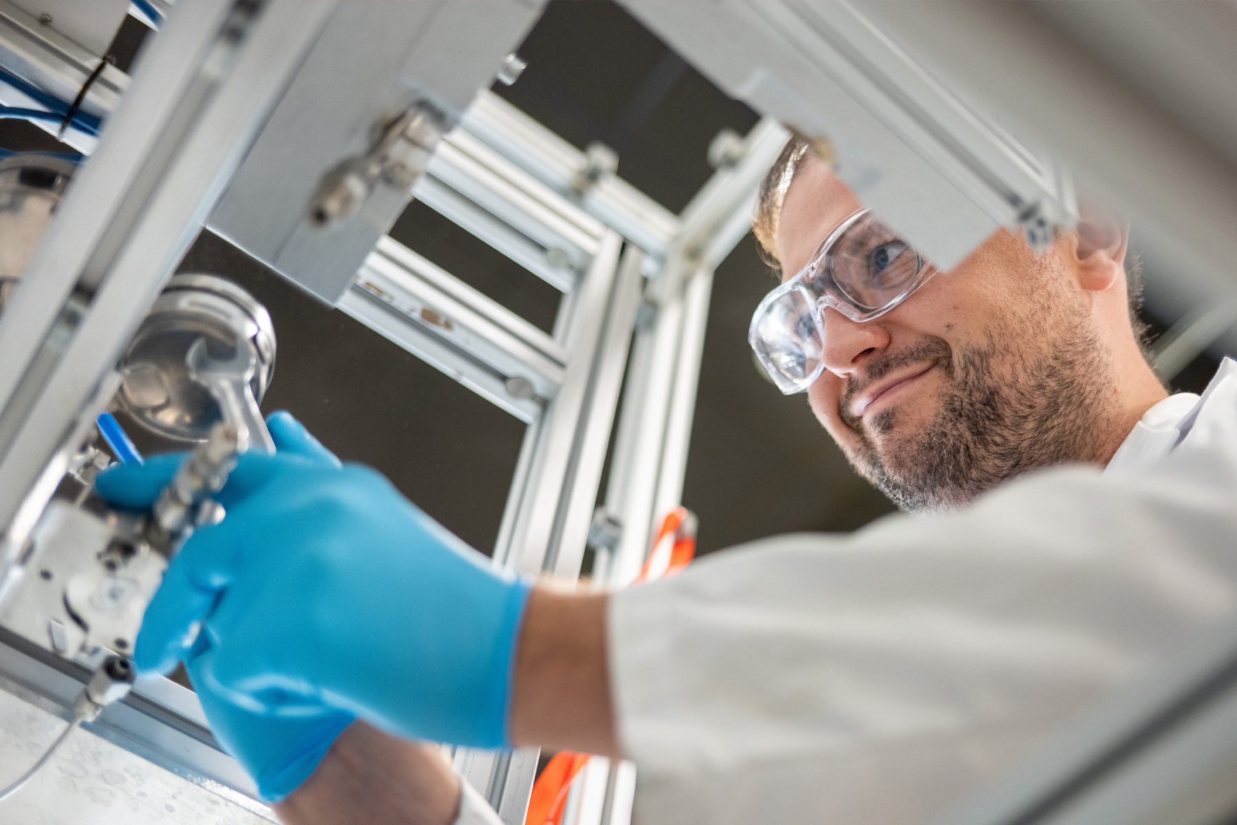 A Greentown member in safety glasses and blue gloves works on a hardware prototype