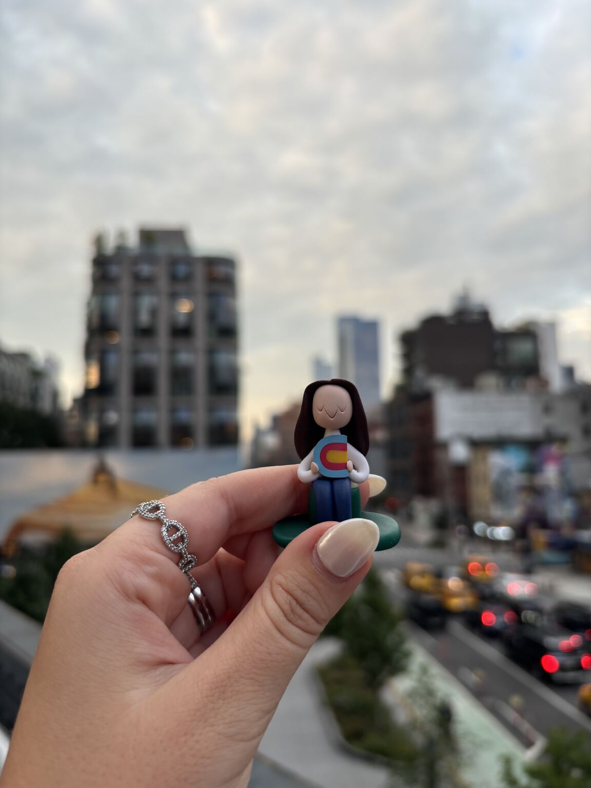 A hand holds Stevenson’s small clay welcome figurine against a blurred city street