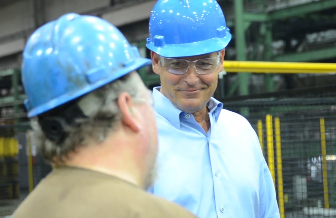 Greg Christopher wearing a blue hard hat and protective glasses while speaking with a colleague at a Mueller plant