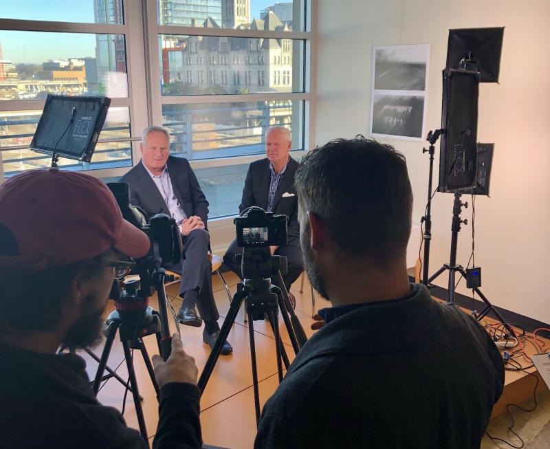 Greg Daily and Rick Stanford seated during an i3 Verticals video shoot, with cameras and production crew in the foreground