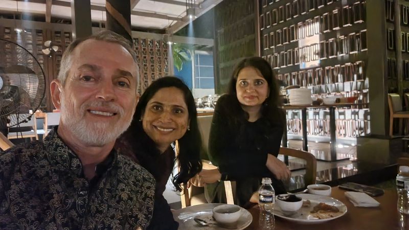 Greg Frick seated at a restaurant table with two fellow diners during his Pune visit