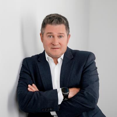 Greg Weston in a dark jacket and white shirt, standing with his arms crossed