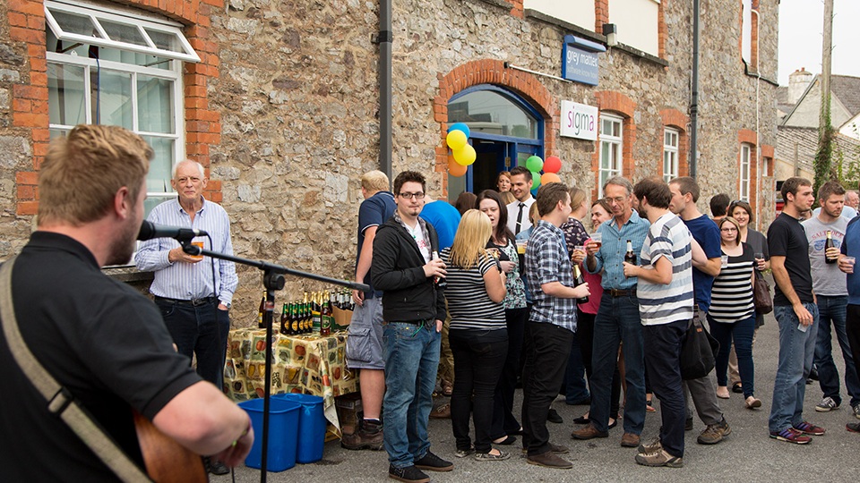 Grey Matter archive staff barbecue outside the stone office building, with a musician in the foreground