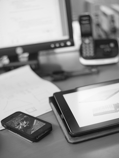Black-and-white desk detail showing a monitor, telephone, tablet and smartphone from Group 22’s team page