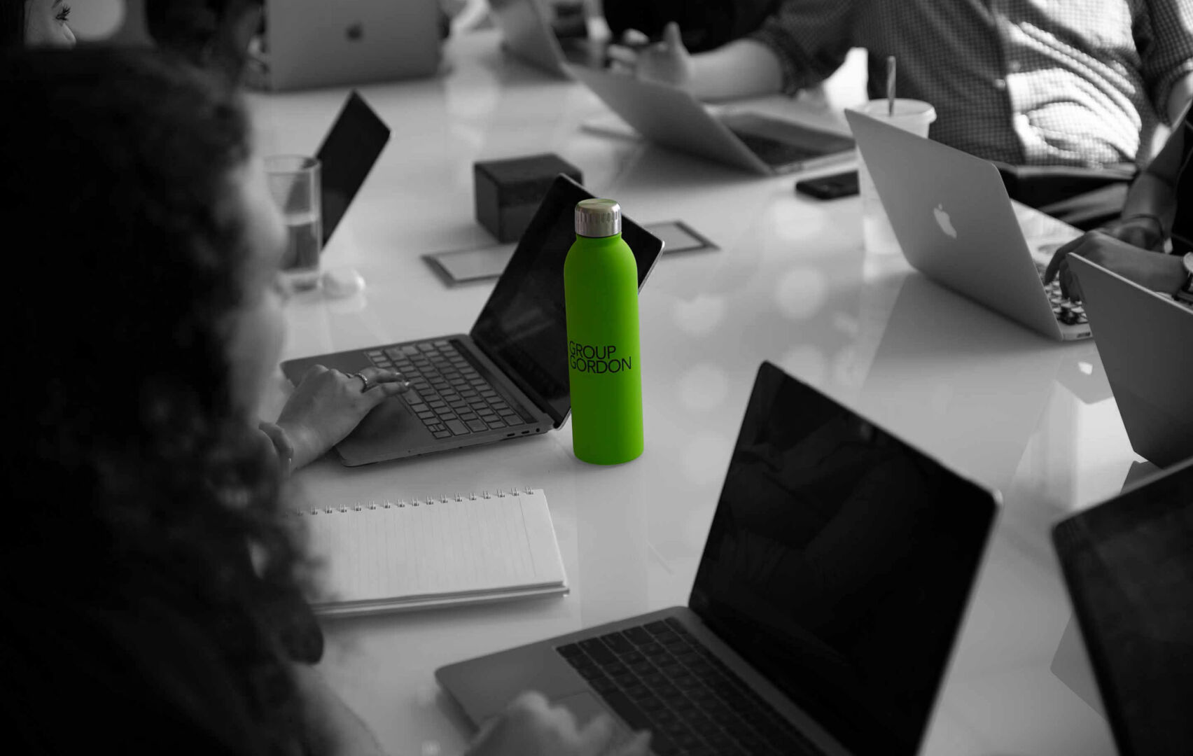 Group Gordon colleagues working around a table with laptops and a bright green branded bottle