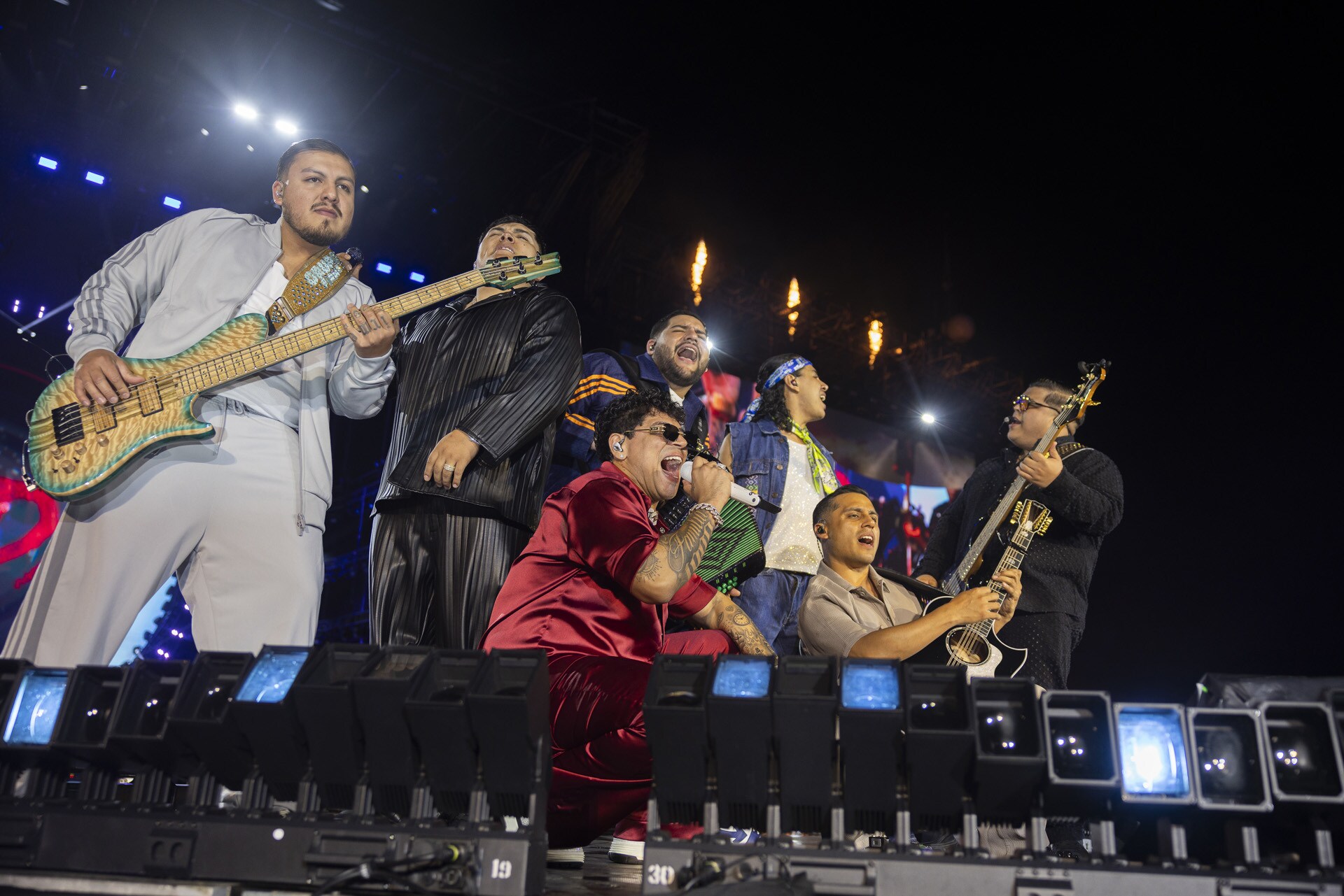 Members of Grupo Firme sing and play instruments together onstage under concert lights