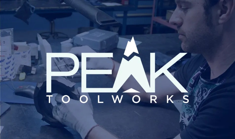 A gloved worker handling a mechanical part at a workbench in the Peak Toolworks customer image