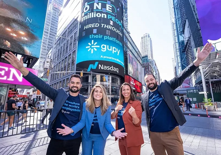 Gupy’s four co-founders in Times Square beside a display celebrating one million hires