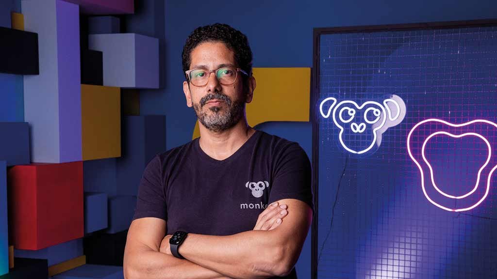 Gustavo Muller Medeiros standing with folded arms beside Monkey’s illuminated monkey mascot