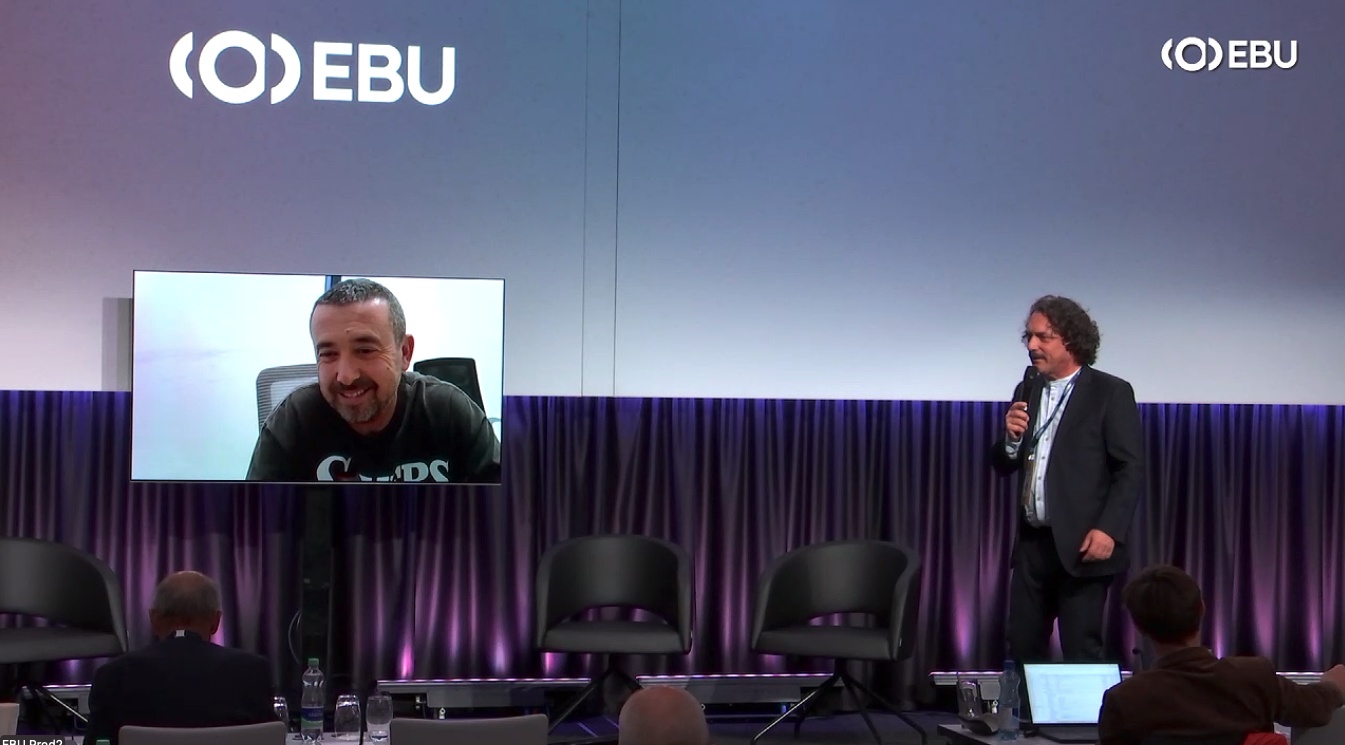 Guy Edri appears by video on an EBU stage screen beside a moderator holding a microphone