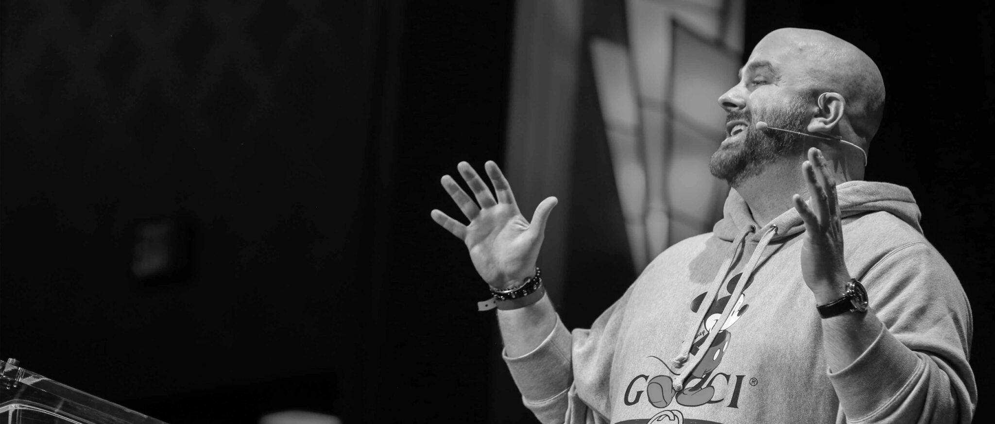 Guy Gal speaking onstage with a headset microphone, hands raised