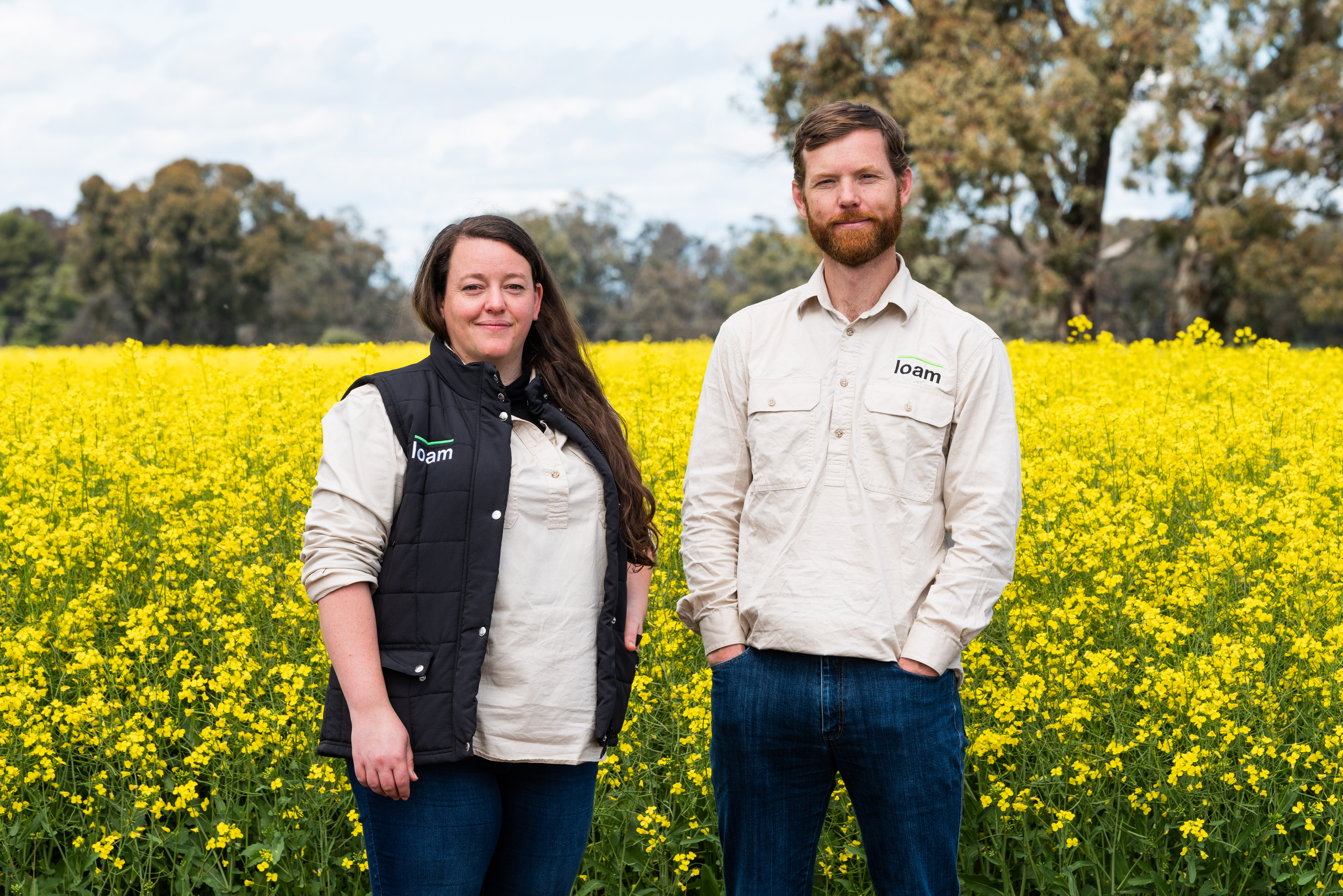 Loam Bio co-founders Tegan Nock and Guy Hudson standing in a flowering canola field
