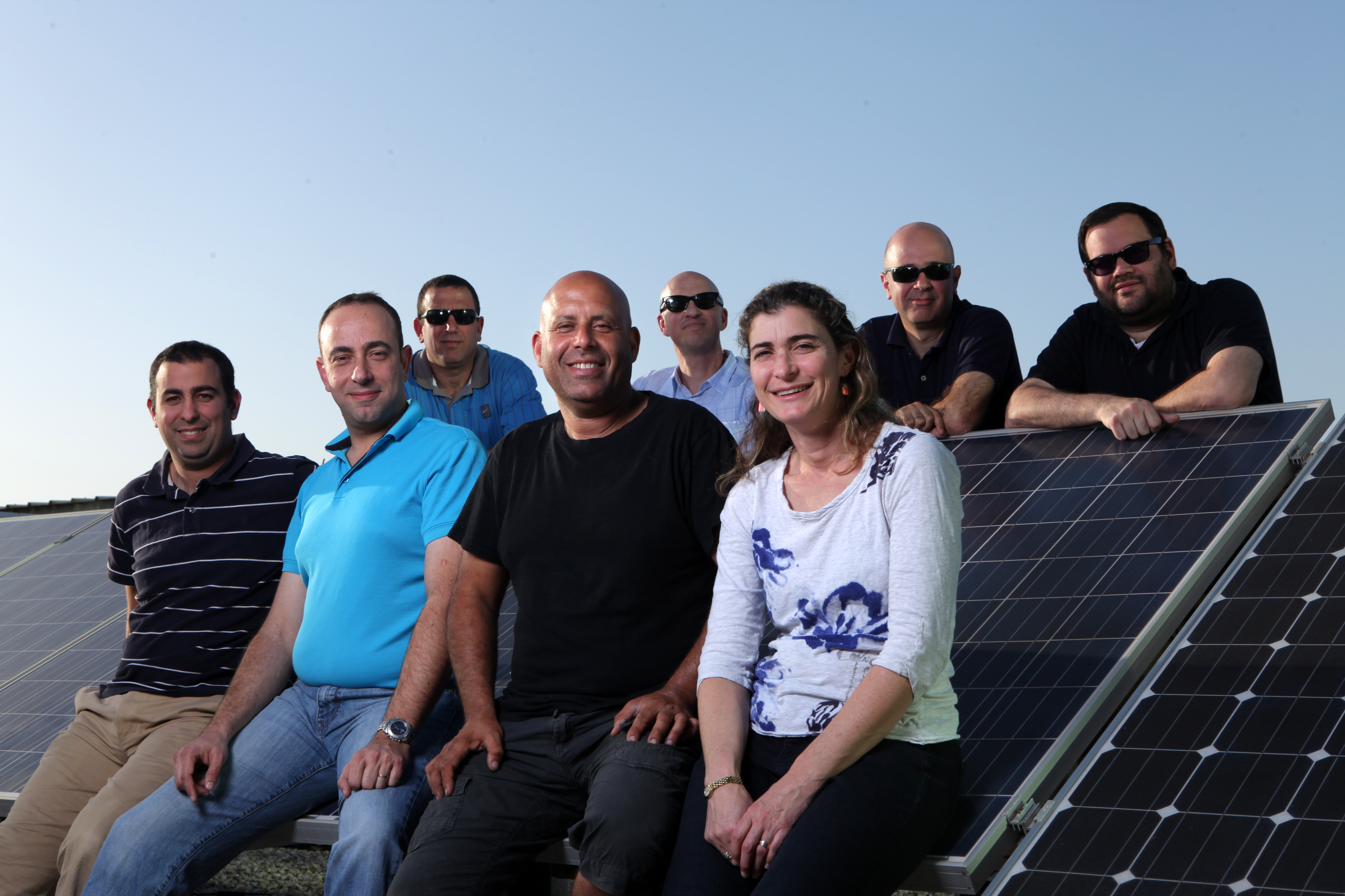 Guy Sella, seated near the center in a black T-shirt, with SolarEdge colleagues beside solar panels