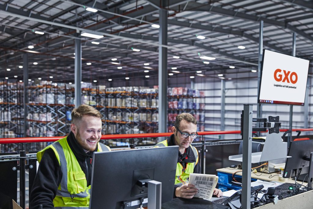 Two GXO warehouse colleagues examine information at a computer workstation