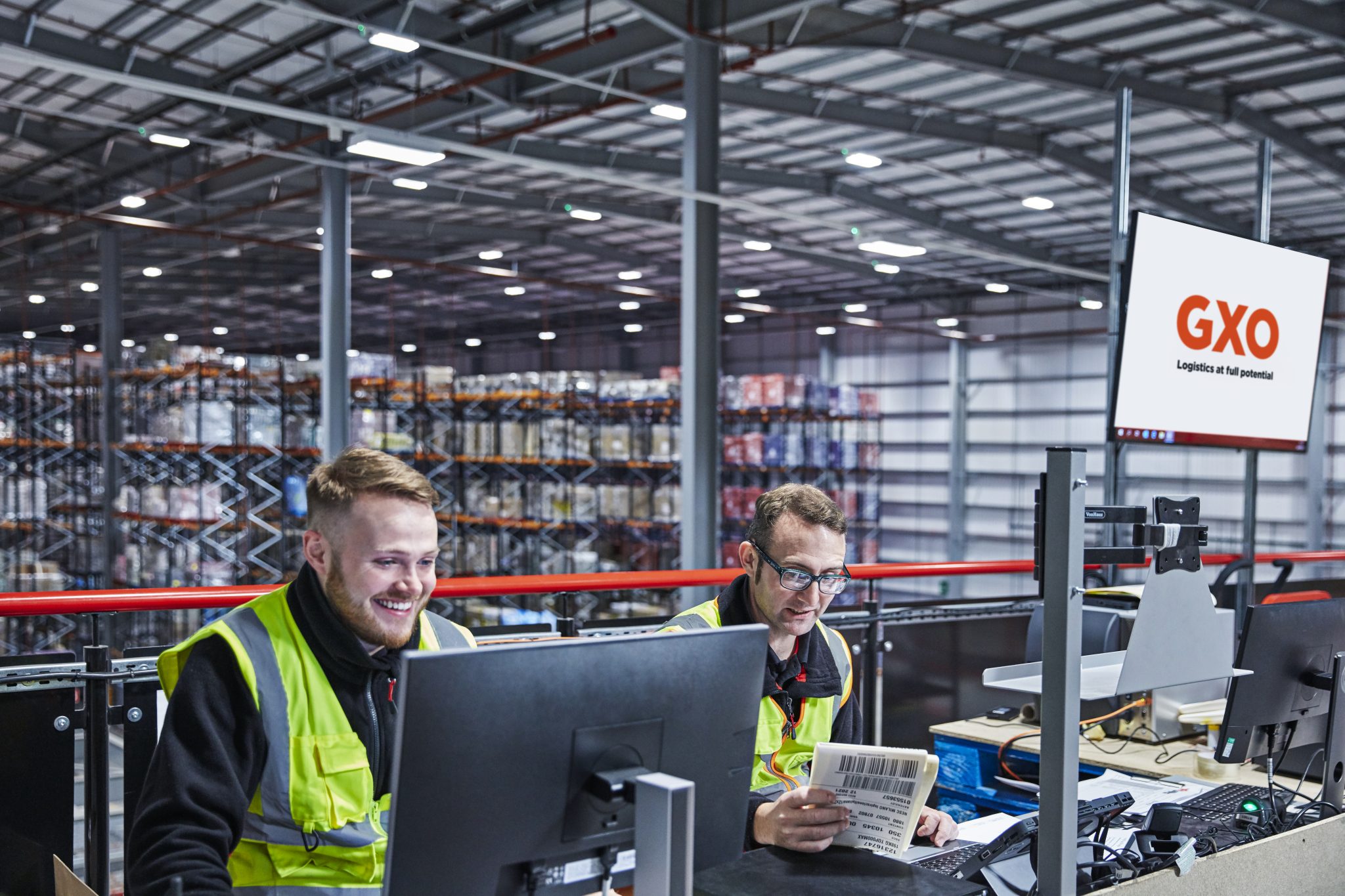 Two GXO warehouse employees working at computer stations and handling shipping labels