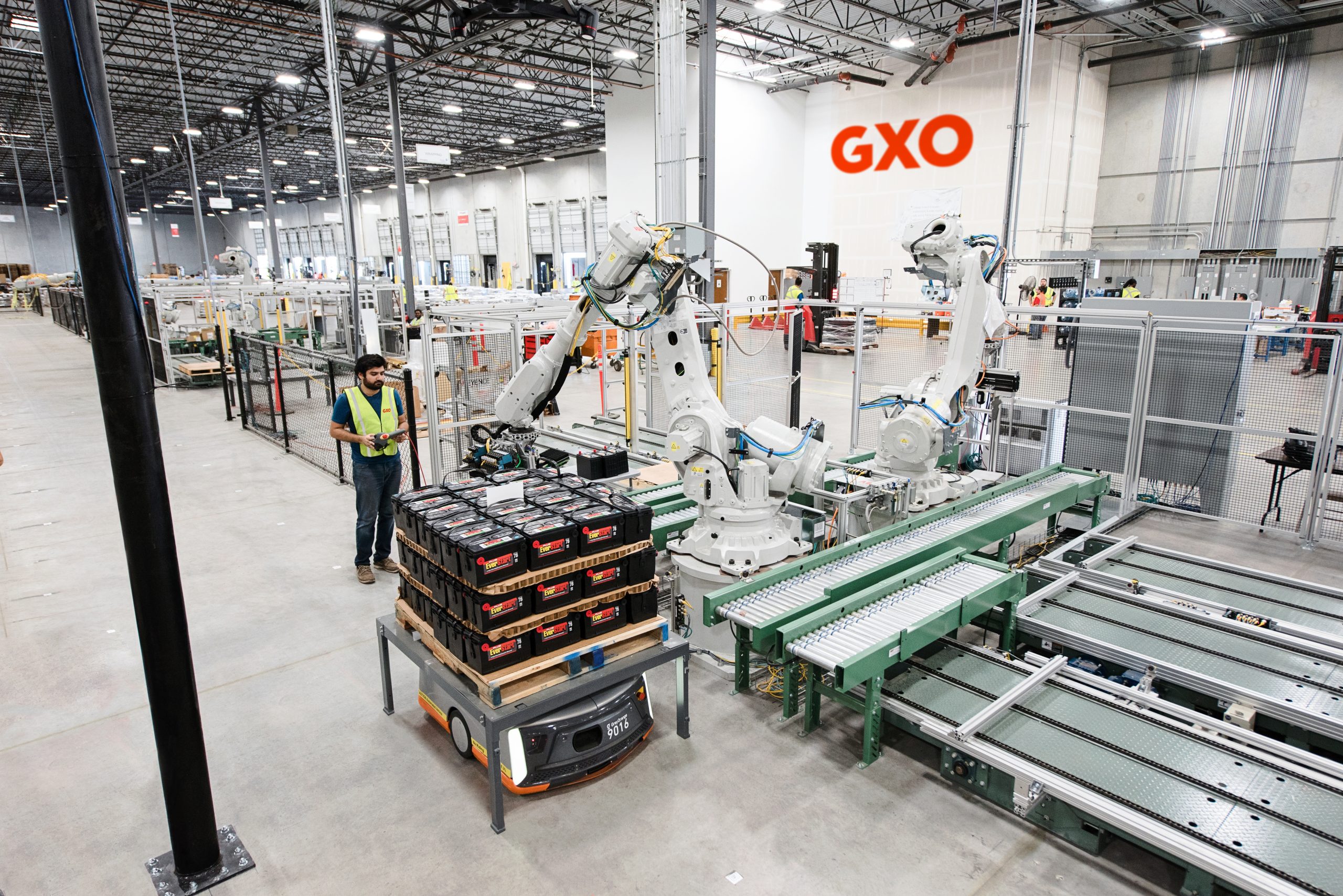A GXO employee beside industrial robotic arms, a mobile platform and a conveyor