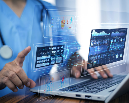 A clinician points toward healthcare analytics displayed over a laptop