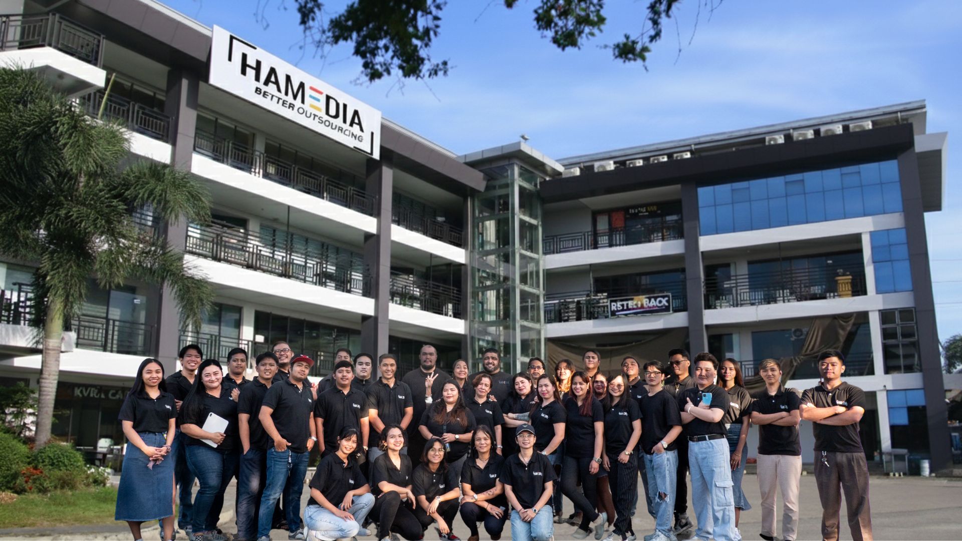 Hamedia team members gathered outside a building displaying the company sign