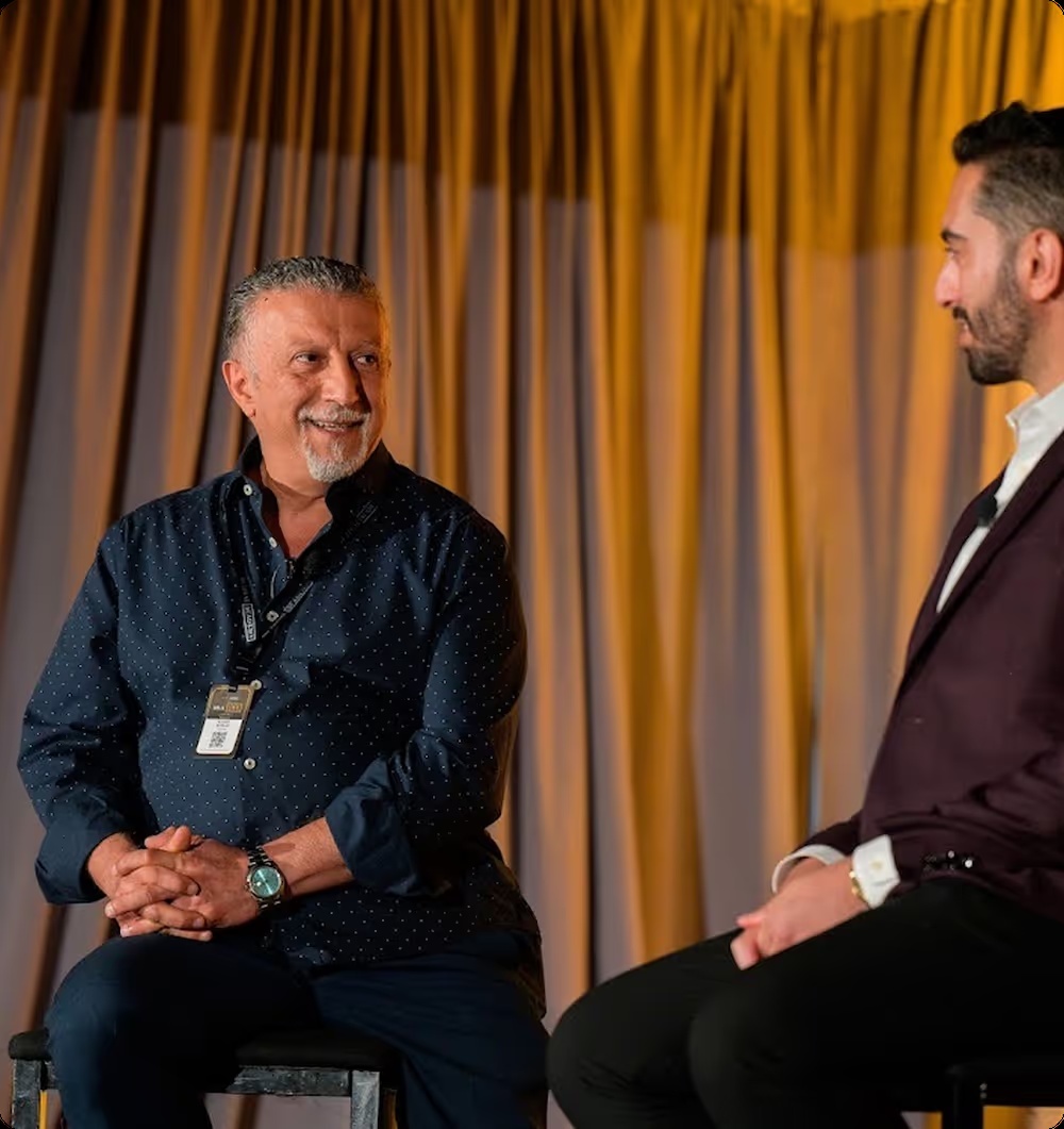 Hamid Kohan seated in conversation with another speaker at a conference