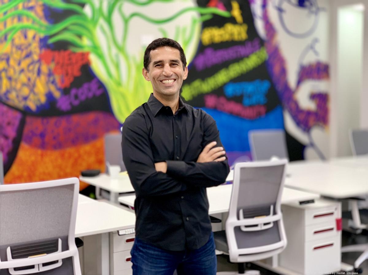 Hamid Shojaee standing among office desks, with a colorful mural behind him