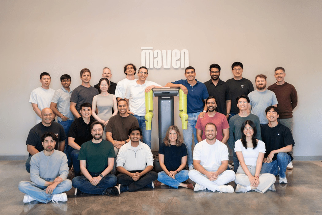 Members of the Maven Robotics team gathered around a green-armed robot