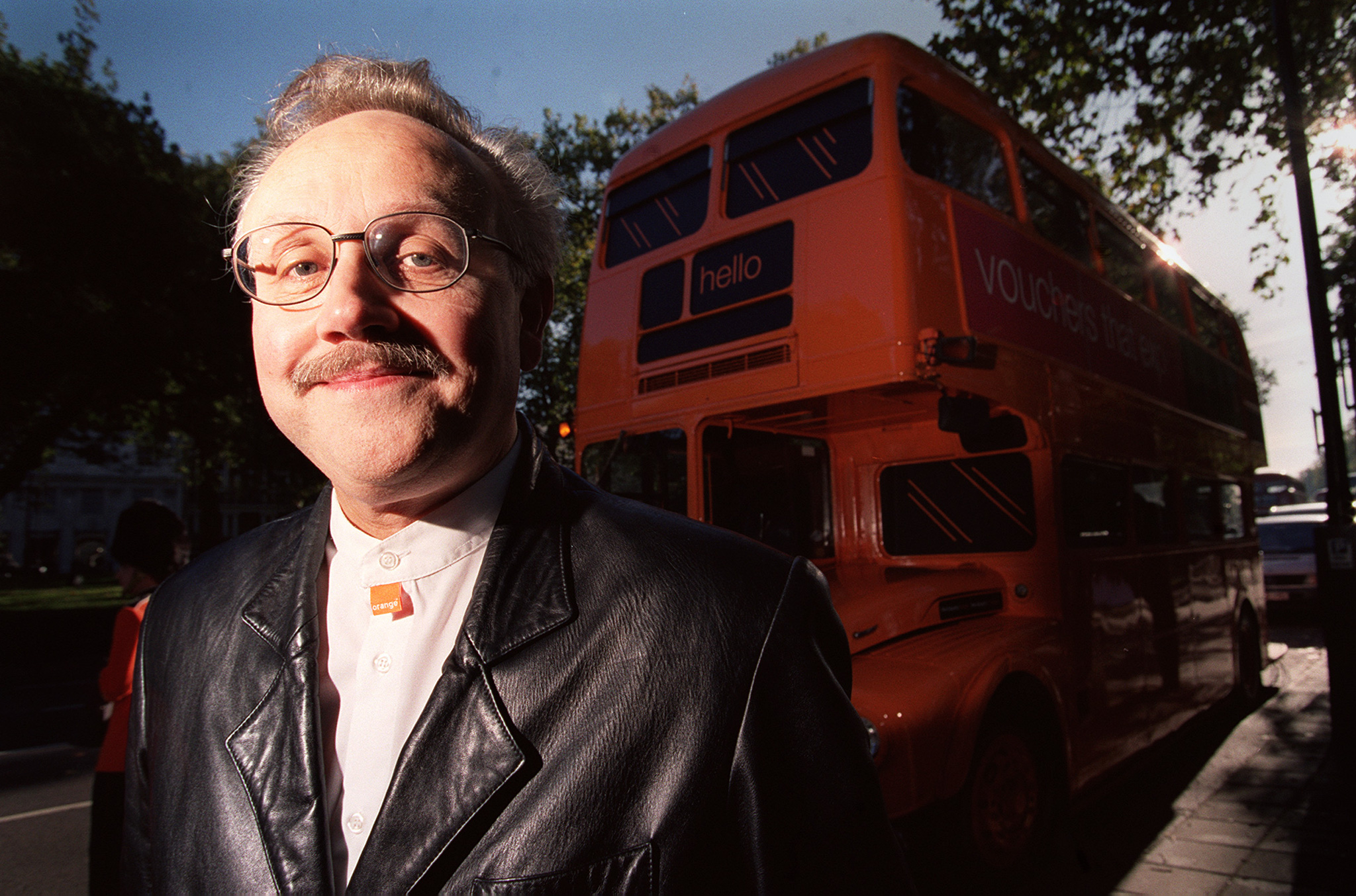 Hans Snook in a leather jacket beside an orange promotional double-decker bus