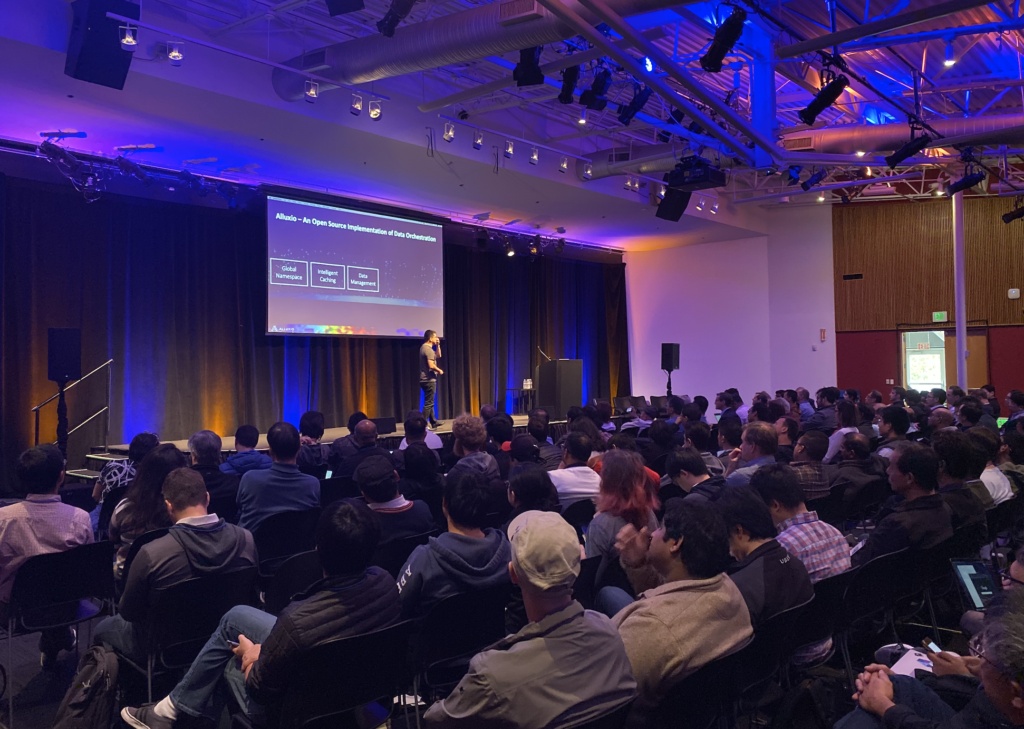 Haoyuan Li addressing an audience beneath an Alluxio architecture slide at the 2019 Data Orchestration Summit